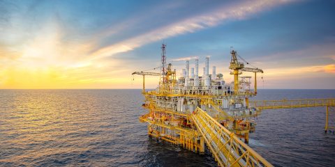 An offshore production rig comprised of yellow girders set against a calm sea with the sun setting behind it.