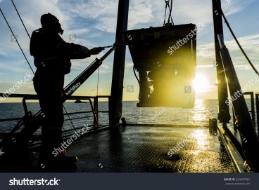 Photo silhouette of worker recovering robotics remote operated vehicle ROV after entering sea surface.