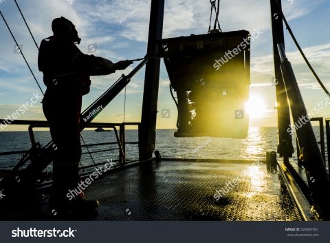 Photo silhouette of worker recovering robotics remote operated vehicle ROV after entering sea surface.