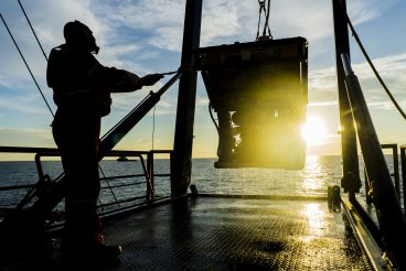 Photo silhouette of worker recovering robotics remote operated vehicle ROV after entering sea surface.