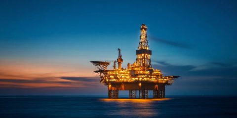 An offshore oil rig lit up against darkening sky after sunset against calm seas.